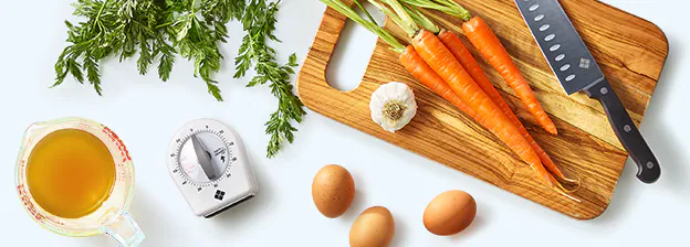 fresh carrots and garlic on a cutting board, broth, eggs and a kitchen timer on the counter
